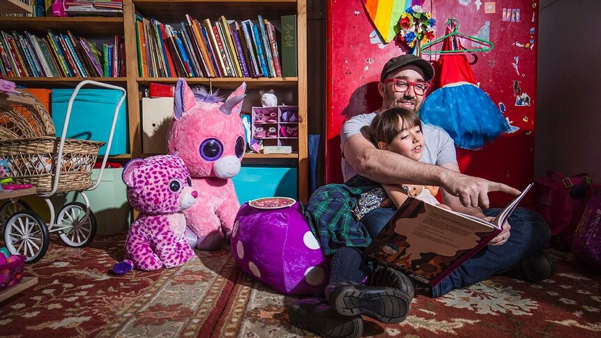 Father and daughter reading a book in a child's bedroom.