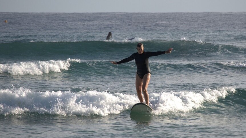 A woman surfing upright on board as it approaches a beach.