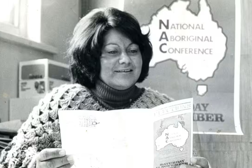 Shirley Peisley looking at a brochure with a sign behind her that says National Aboriginal Conference