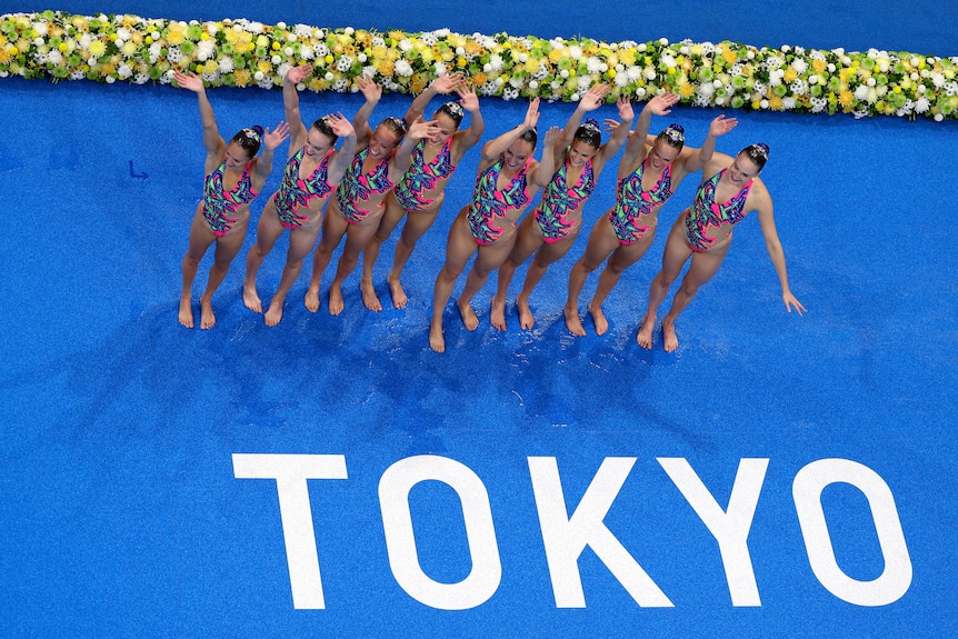Canada's artistic swimming wave after their routine. The word TOKYO is written on the floor in front of them.