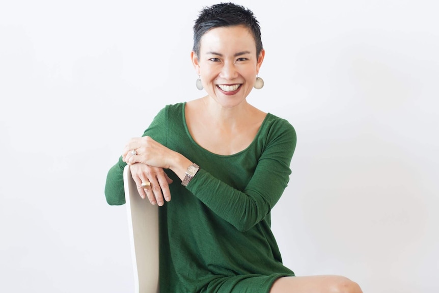 A professional photo of Dr Li-Chuen Wong smiling in a green dress and posing on a chair. 
