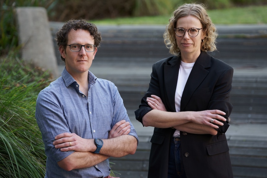 A young man and women, both wearing glasses, stand with arms crossed 