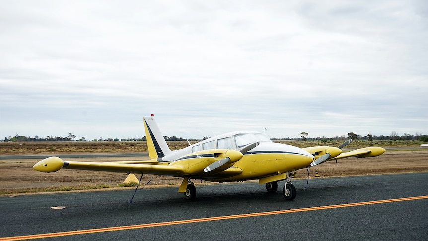 A twin-engine plane sits on the tarmac of a small country airfield.