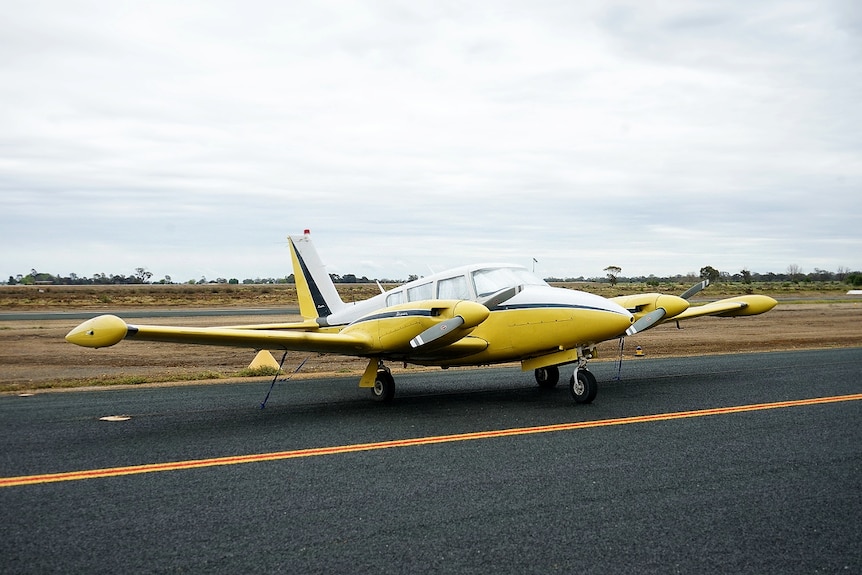 A twin-engine plane sits on the tarmac of a small country airfield.