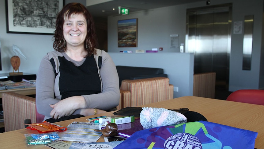 Woman sits at back of table with contents of a carer's bag displayed on the table in front of her.