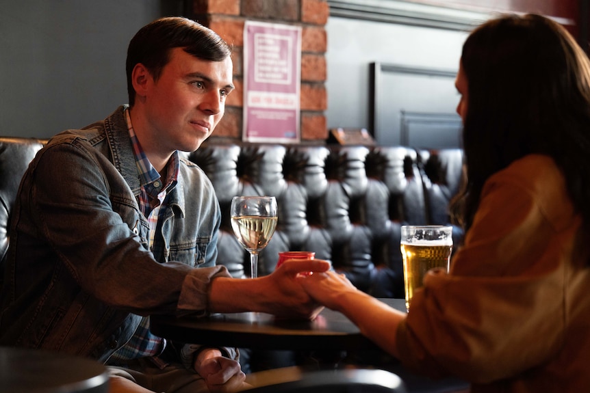 A young man and woman in a bar/pub holding hands while enjoying a drink.