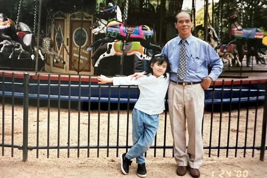 An old photo of Annie and her dad David in front of a carousel.