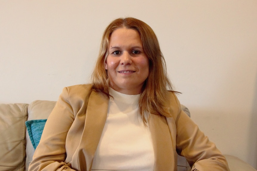  A woman with warm blonde hair and a cream blazer on looks at the camera 