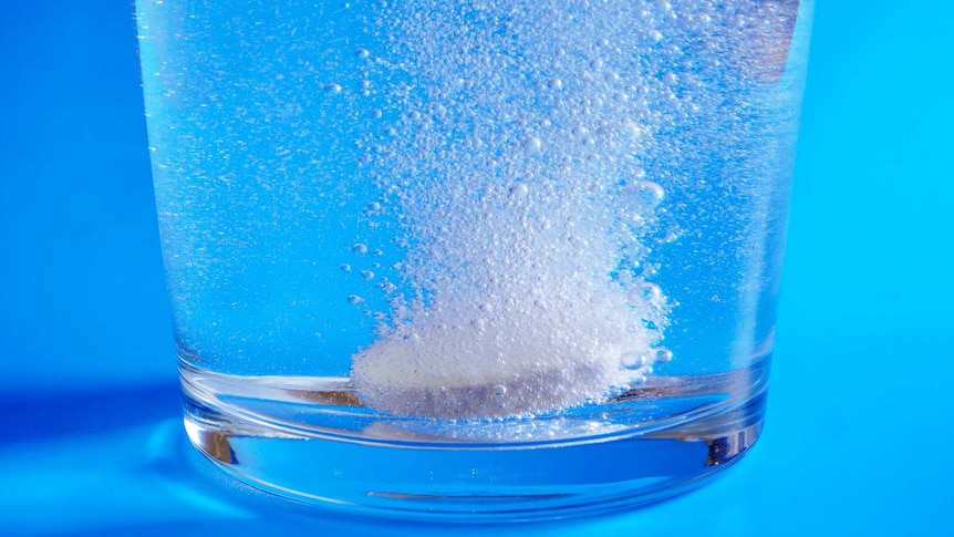 Closeup of effervescent tablet dissolving in glass of water on blue background
