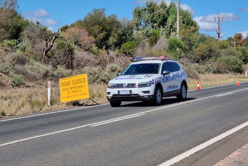 A police car parked near a road block on a country road on a sunny day.