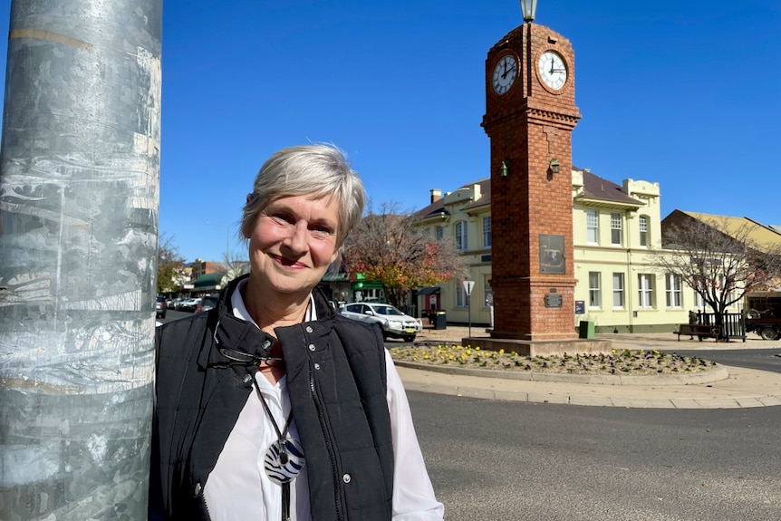 A woman smiling at the camera with a town clock in the background.
