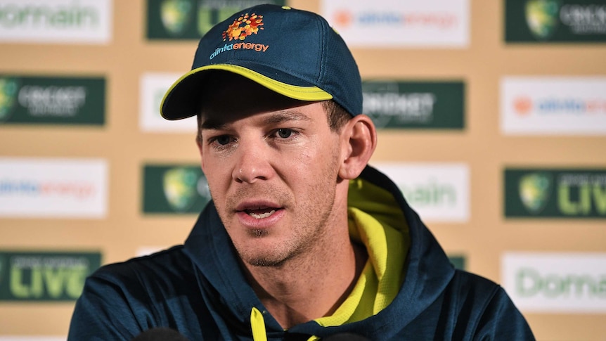 An Australian cricketer sits behind a bank of microphones talking to the media.