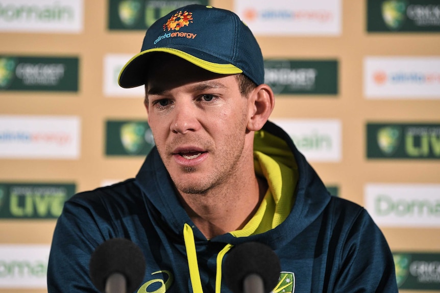 An Australian cricketer sits behind a bank of microphones talking to the media.