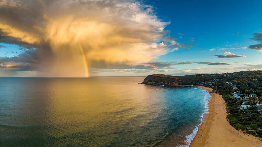 Sun-drenched cloud with rainbow rests just off shore