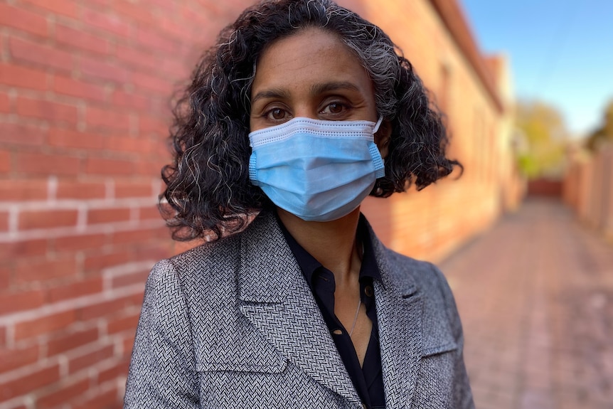 A woman wearing a mask standing behind a brick wall. 