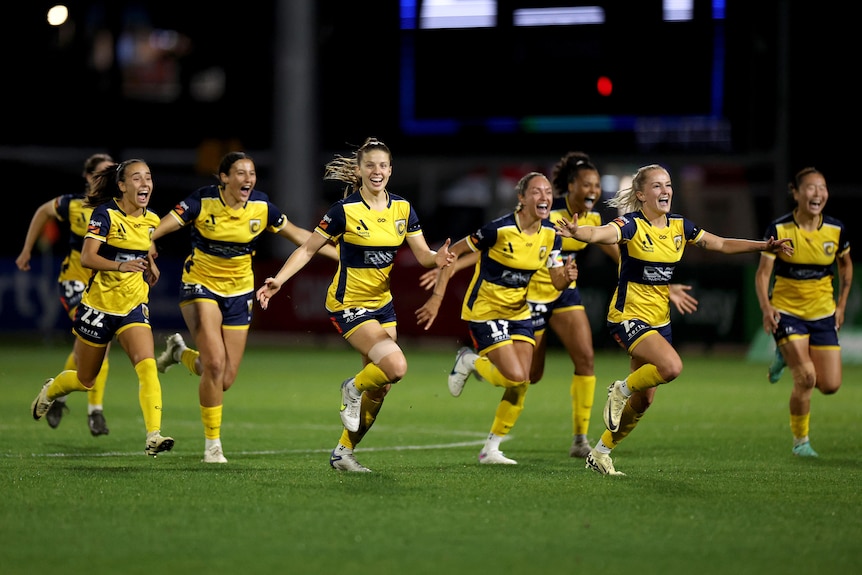 A women's soccer team wearing yellow and dark blue run in a line towards a team-mate after winning a match