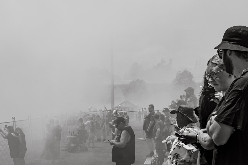 A big crowd watches burnouts through a cloud of smoke.