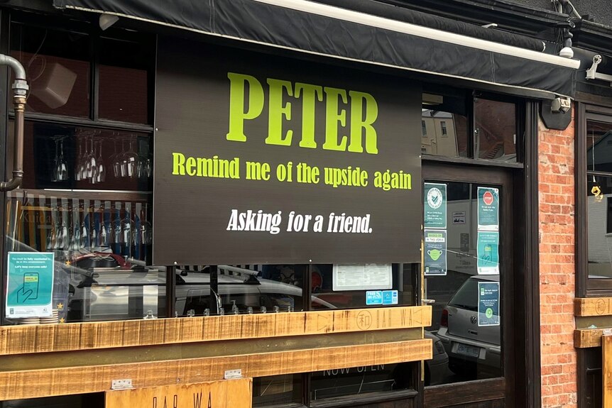 Signs on the windows of a bar saying: "Peter, remind me of the upside again. Asking for a friend."