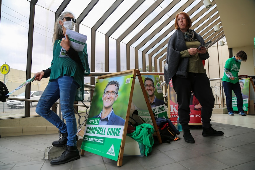 A Greens campaigner hands out a flyer, standing in front of a Campbell Gome for Northcote sign.