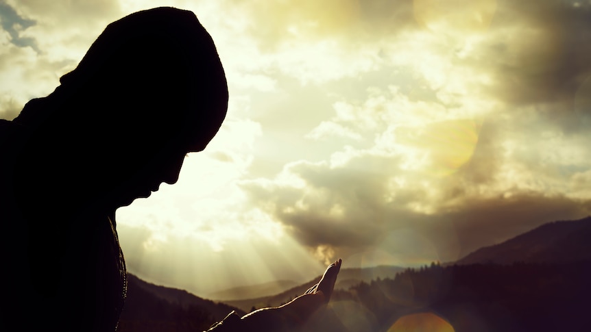 A person stares down at their hands while perched on a mountain.