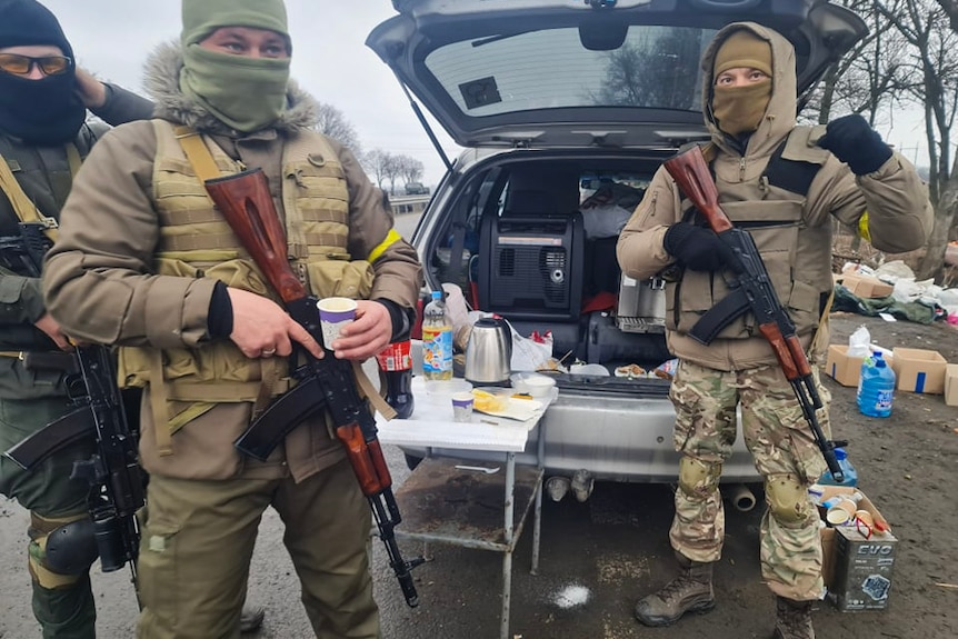 Soldiers standing in front of a car drinking coffee.