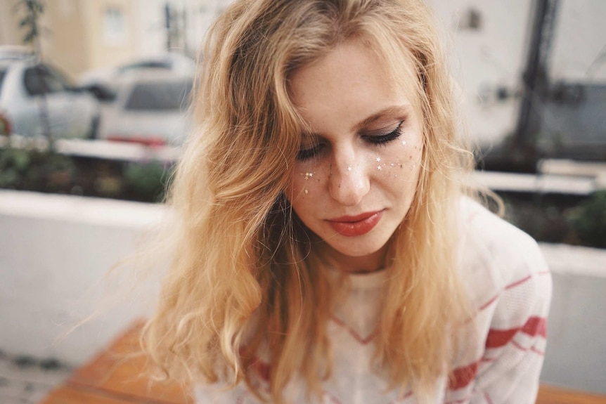 Young blonde woman with looks down, with star-shaped glitter on her cheeks, to depict making your skincare regime eco friendly