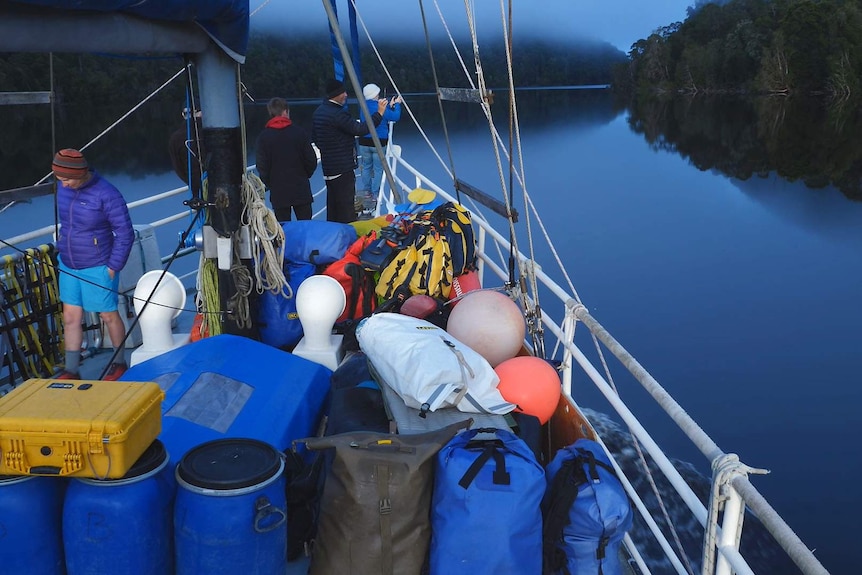 Watertight barrels, bags and lifejackets on the deck as the yacht cuts through a perfect mirror still dawn.
