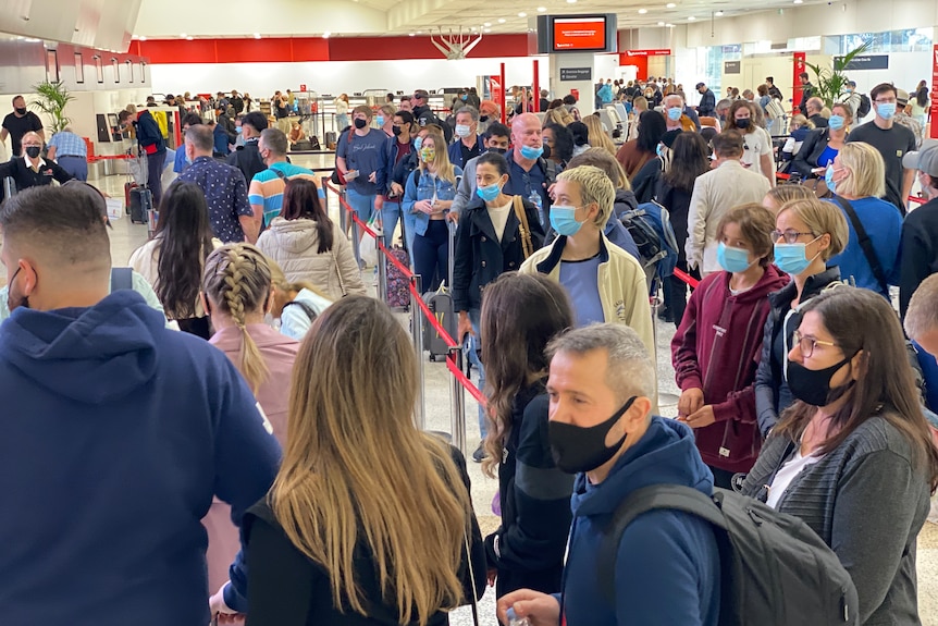 A queue of travellers at an airport, all wearing face masks.