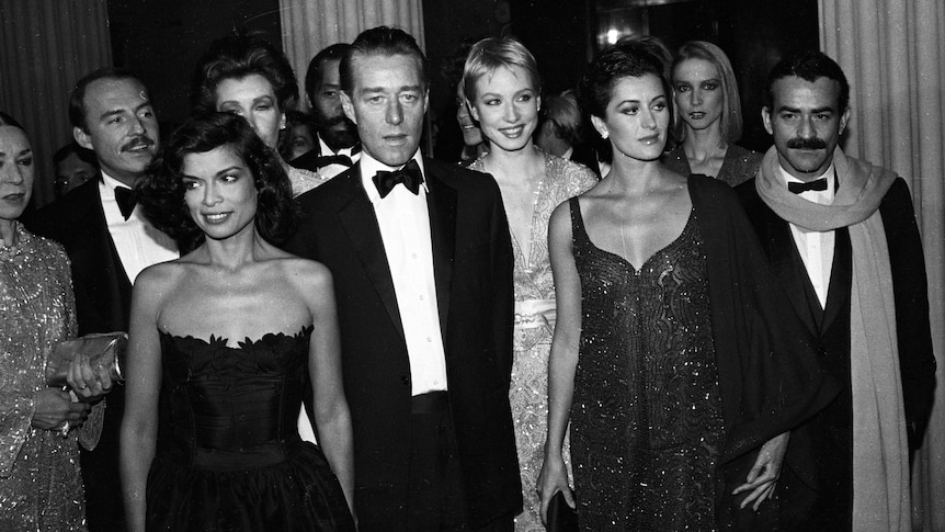 A black and white photo of men in tuxedos and women in gowns