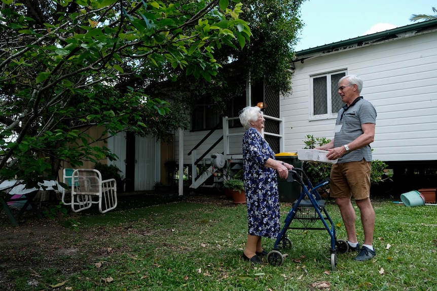 Irene and Chris stand talking to each other under a tree. 