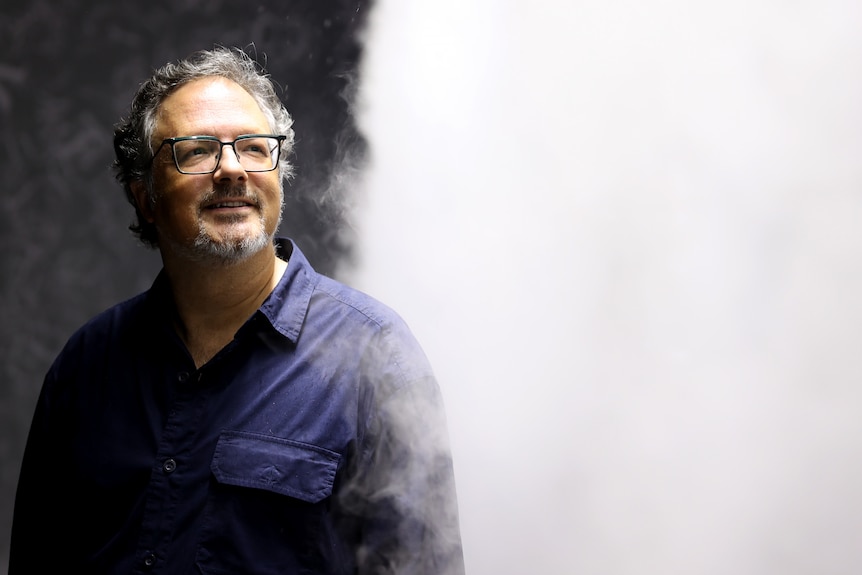 Rafael Lozano-Hemmer, a middle-aged Mexican man with greying hair, moustache and beard wears a navy shirt in a vapour cloud.