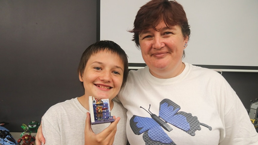 A teenage boy and a woman smiling and holding up Lego.