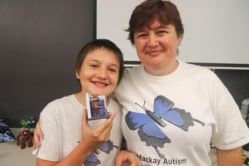 A teenage boy and a woman smiling and holding up Lego.