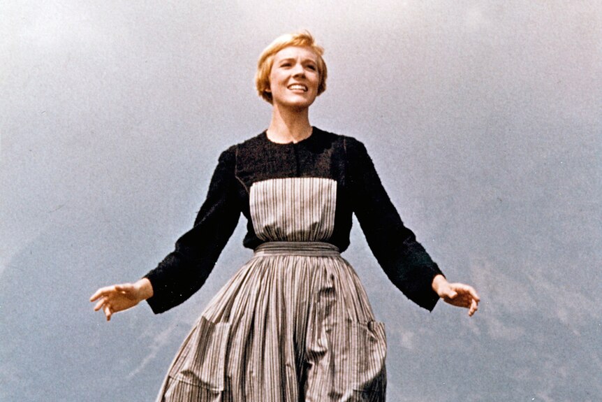A young Julie Andrews in the sound of music standing on a foggy hill with her arms outstretched.