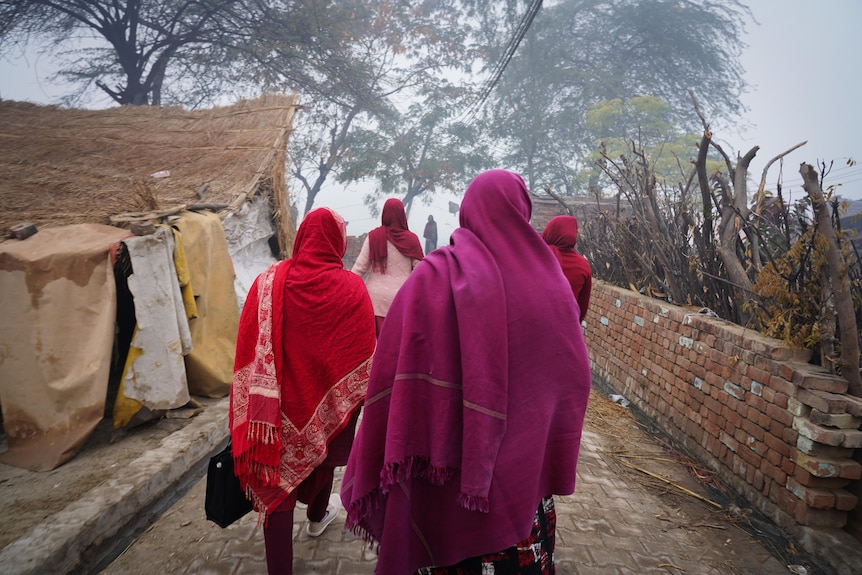 A group of women wearing maroon and pink robes walks down a steep street on a foggy morning