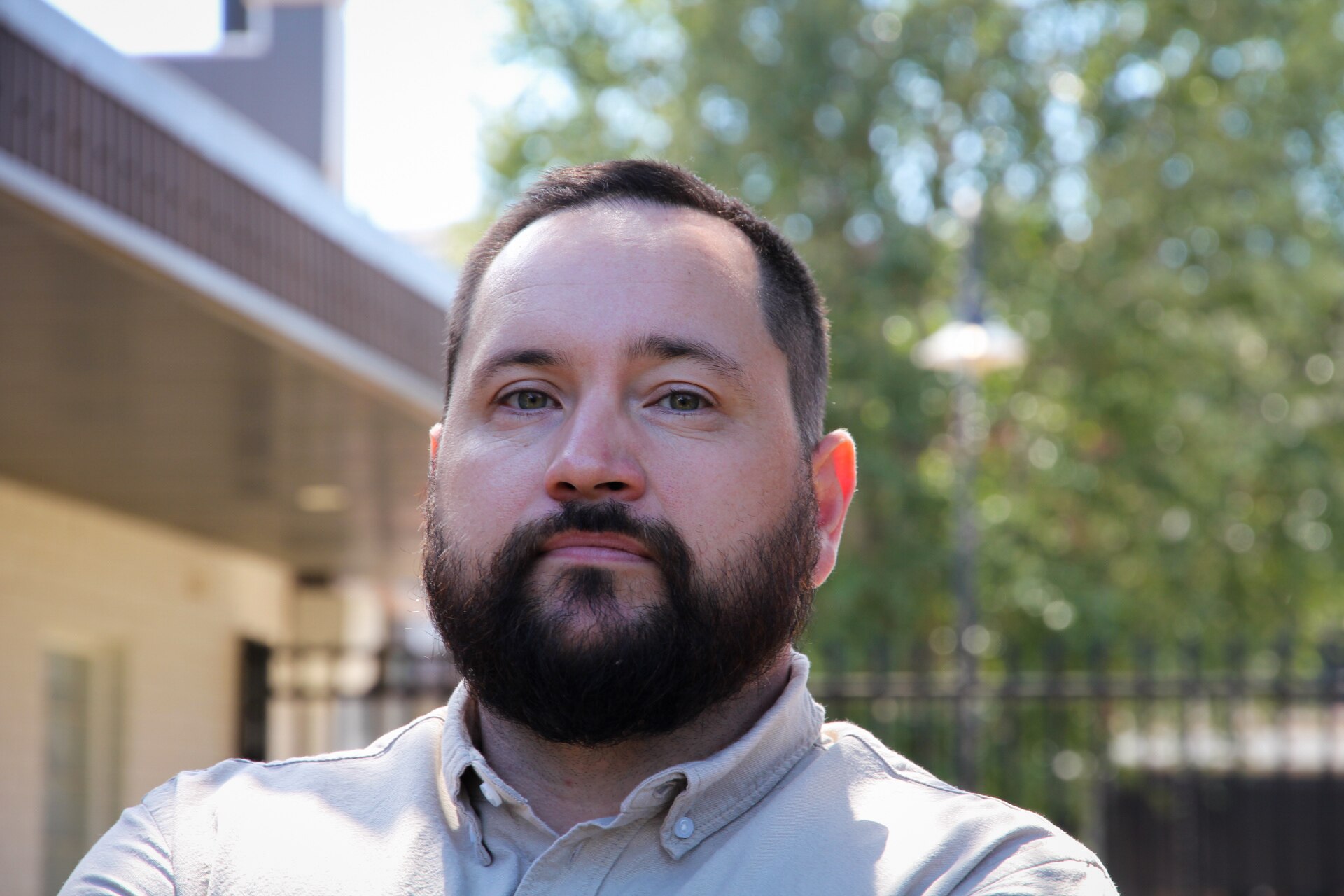 A bearded man in a cream shirt stands in front of a green background