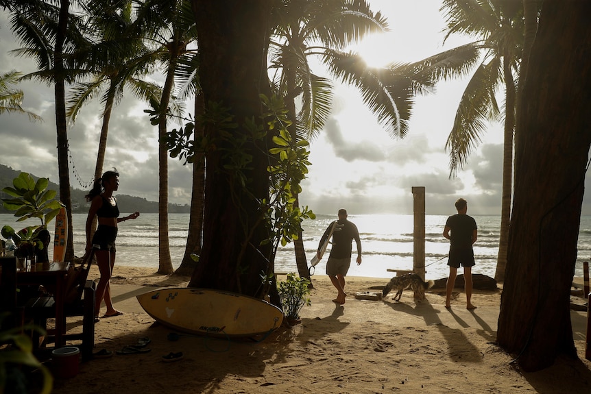 Several people walk around a beach as the sun rises 