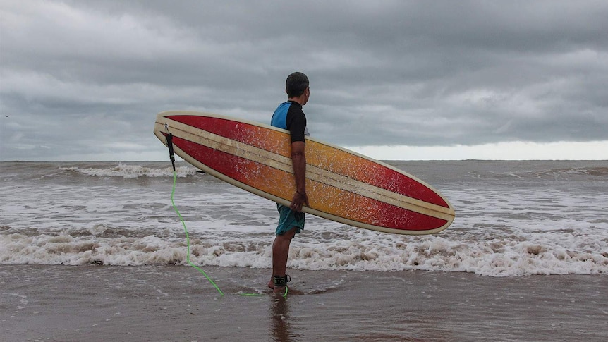 surfer with her board looking over beach at stormclouds