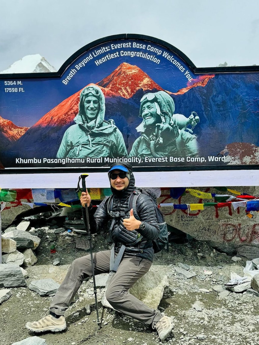 Ram Khanal smiles and gives the thumbs up in front of a sign at Mount Everest base camp.