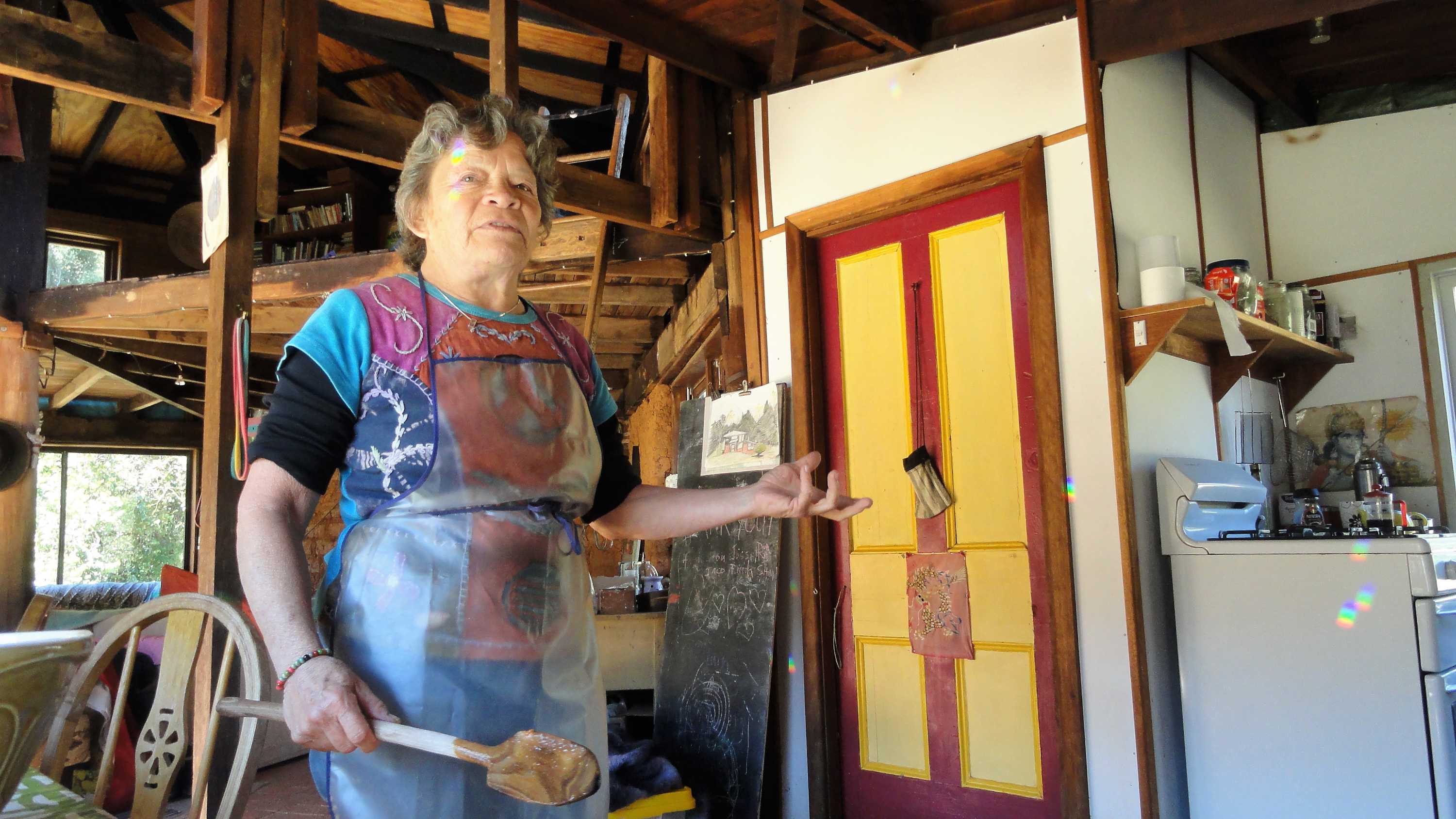 Medium shot of a woman standing in a kitchen holding a wooden spoon.
