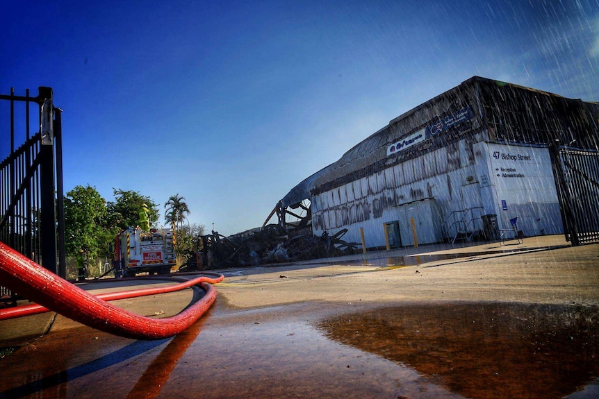 A firehose is pictured in the foreground with the warehouse behind