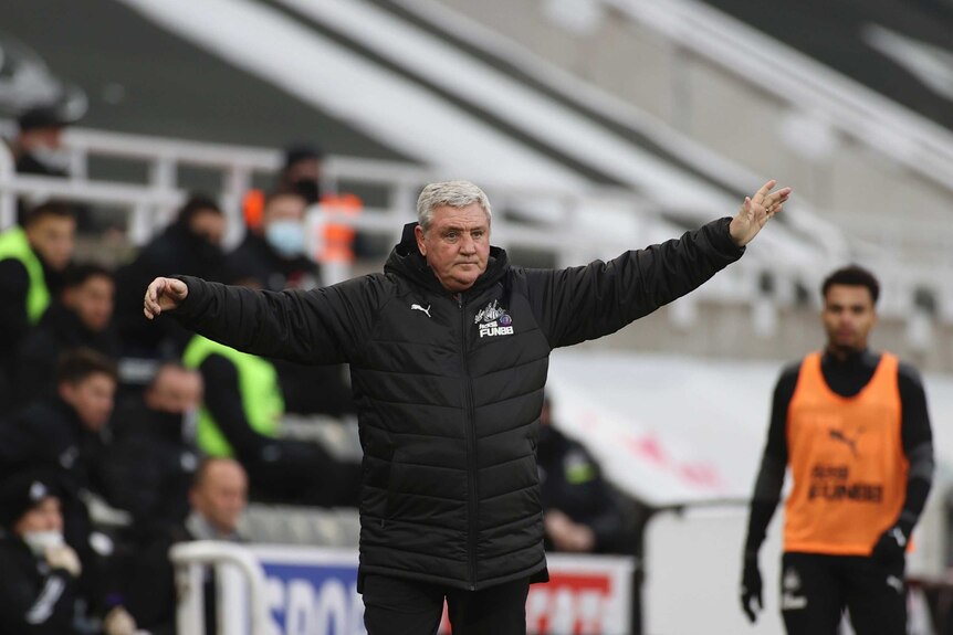 A man wearing a black coat holds out his arms.