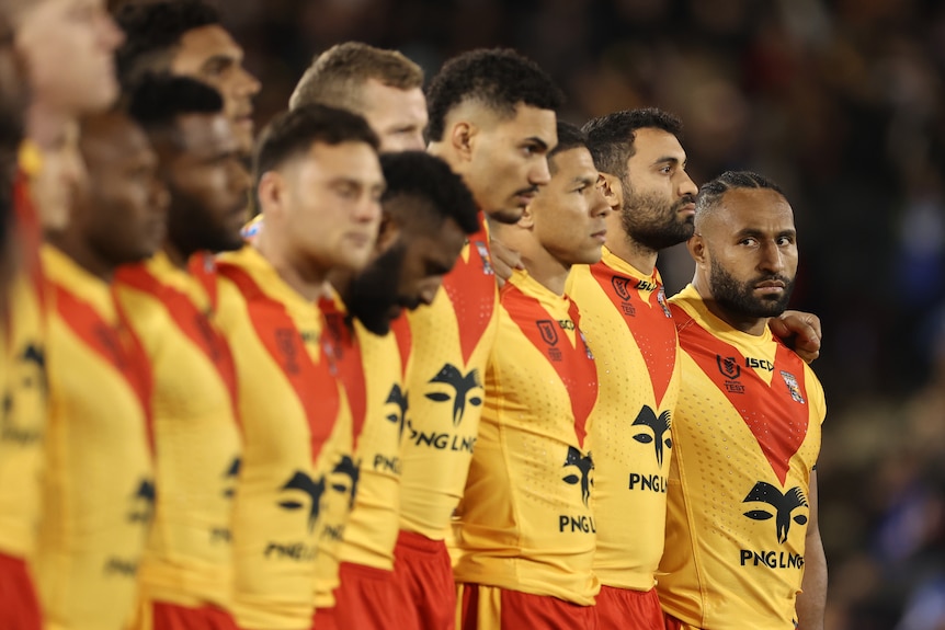 A line up of footballers in red and yellow jerseys ending with one man looking at the camera