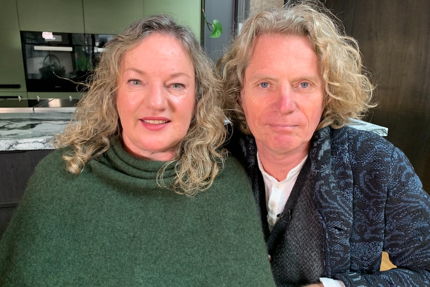 A woman and man both with curly blonde hair sit in a kitchen