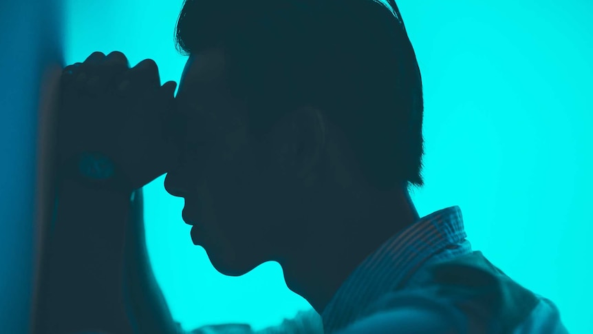 Silhouette of a man leaning on a wall against an aqua background to depict the pain and experience of living with migraines.