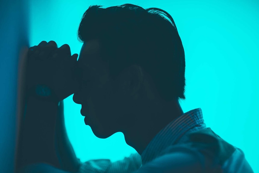 Silhouette of a man leaning on a wall against an aqua background to depict the pain and experience of living with migraines.