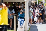 People wearing masks waiting outside, and under a tent.