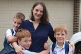 A mum stands on her driveway cuddling 3 primary school-aged boys