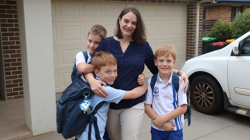 A mum stands on her driveway cuddling 3 primary school-aged boys