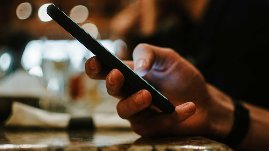 A male hand holds a mobile phone viewed from the side.